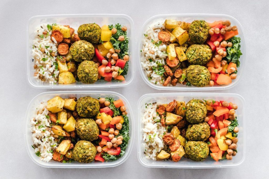 Dieta pudełkowa bez glutenu i laktozy w estetycznym wydaniu. Cztery plastikowe pojemniki z gotowymi posiłkami ustawione obok siebie na jasnym tle.