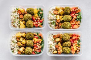 Dieta pudełkowa bez glutenu i laktozy w estetycznym wydaniu. Cztery plastikowe pojemniki z gotowymi posiłkami ustawione obok siebie na jasnym tle.