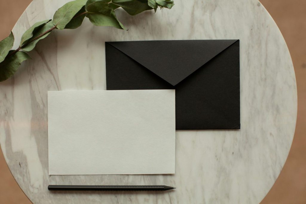 Elegancka czarna koperta i biała karta na marmurowym blacie, prezentujące nowoczesne czarne zaproszenia ślubne w stylu minimalistycznym.