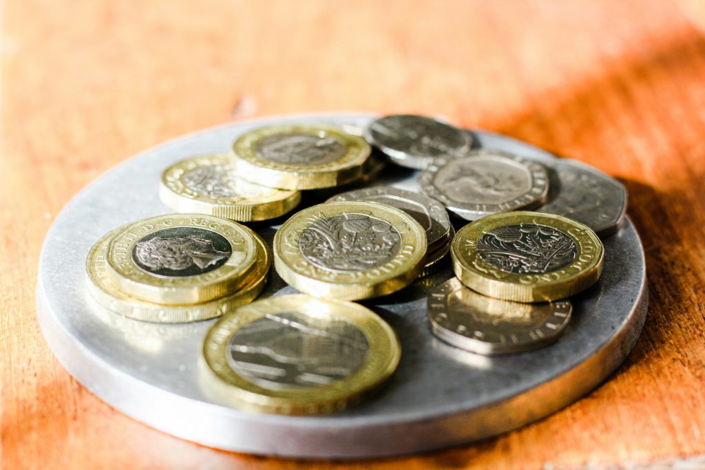 Różne monety ułożone na okrągłej metalowej podstawce stojącej na drewnianym blacie, symbol oszczędzania i domowych finansów