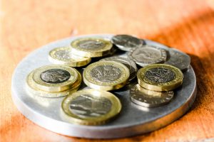 Różne monety ułożone na okrągłej metalowej podstawce stojącej na drewnianym blacie, symbol oszczędzania i domowych finansów