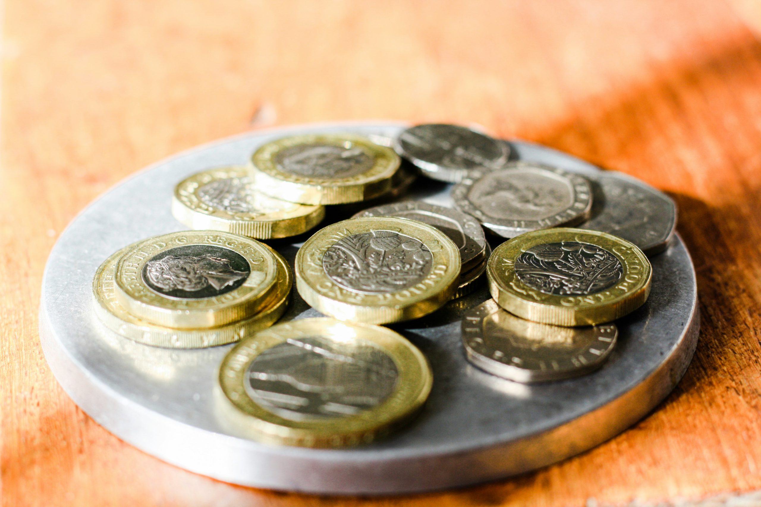 Różne monety ułożone na okrągłej metalowej podstawce stojącej na drewnianym blacie, symbol oszczędzania i domowych finansów
