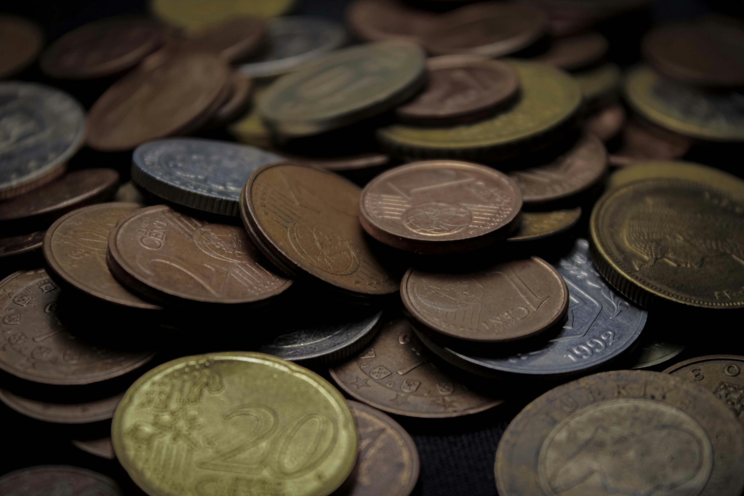 Zbliżenie na rozsypane monety euro o różnych nominałach, ułożone chaotycznie na ciemnym tle, symbol drobnych oszczędności i codziennych wydatków